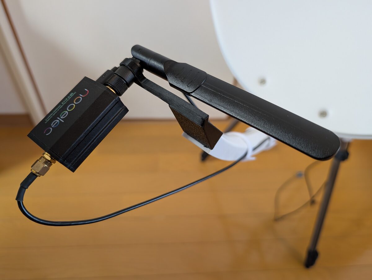 Close-up of the feed: the rod antenna lies on the home-made mount at the end of the feed arm, its connector screwed onto the Nooelec LaNA; a coaxial cable leaves the other side of the amplifier.